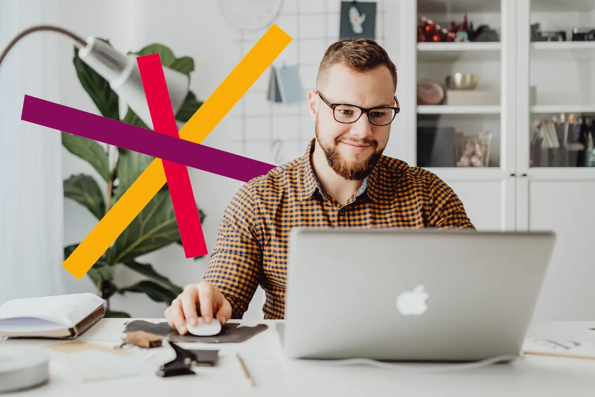 Silmälasipäinen mies istuu pöydän ääressä ja katsoo tietokonetta