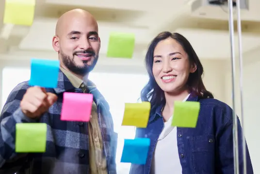 Nainen ja mies katsoo lasiseinää, jossa on post it -lappuja